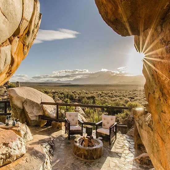 Two chairs and a small fire framed by towering sandstone at sunset