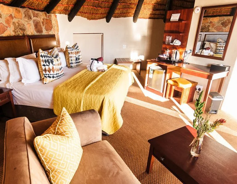 Warm, sunlit Kagga Kamma Hut Suite with a thatched ceiling and patterned cushions